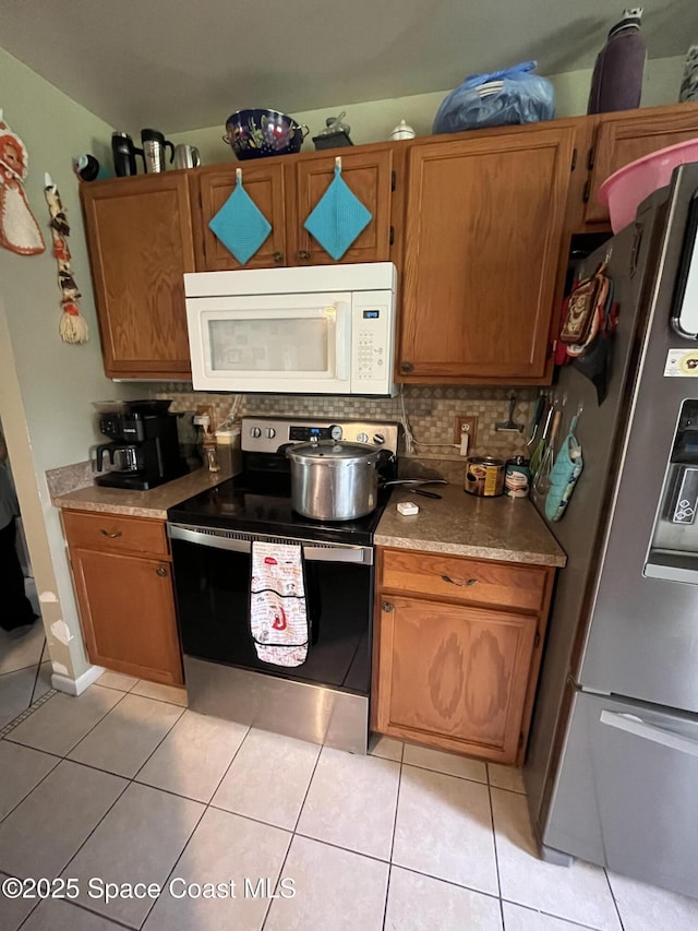 237 Jacaranda Ave NW, Palm Bay, FL 32907 - kitchen featuring appliances with stainless steel finishes, light tile patterned floors, decorative backsplash, and brown cabinetry