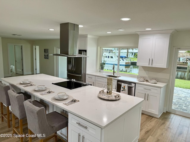 57 Riverview Ln, Cocoa Beach, FL 32931 - kitchen with black appliances, a center island, light wood-type flooring, white cabinets, and island exhaust hood