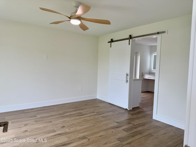 57 Riverview Ln, Cocoa Beach, FL 32931 - unfurnished room with a barn door, ceiling fan, light wood-style flooring, and baseboards