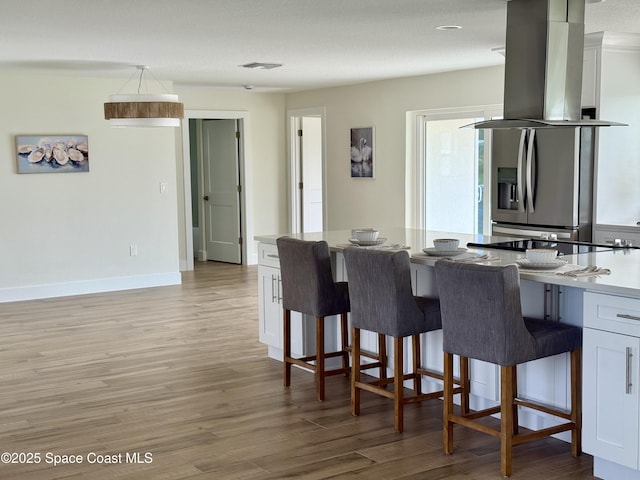 57 Riverview Ln, Cocoa Beach, FL 32931 - kitchen with island exhaust hood, light wood-type flooring, a kitchen breakfast bar, white cabinets, and healthy amount of natural light