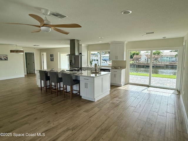 57 Riverview Ln, Cocoa Beach, FL 32931 - kitchen featuring island exhaust hood, white cabinetry, wood finished floors, an island with sink, and a textured ceiling