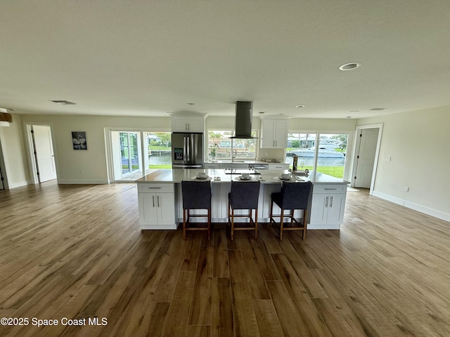 57 Riverview Ln, Cocoa Beach, FL 32931 - kitchen with island range hood, stainless steel refrigerator with ice dispenser, white cabinetry, wood finished floors, and a large island