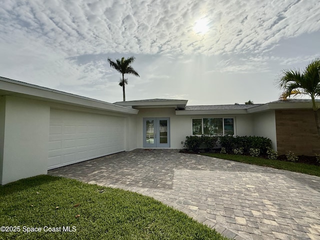 57 Riverview Ln, Cocoa Beach, FL 32931 - view of front of house with stucco siding, french doors, decorative driveway, and an attached garage