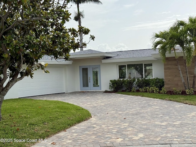 57 Riverview Ln, Cocoa Beach, FL 32931 - view of front of home with stucco siding, french doors, driveway, a garage, and a front yard