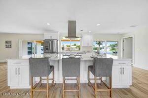 57 Riverview Ln, Cocoa Beach, FL 32931 - kitchen with wall chimney range hood, stainless steel refrigerator with ice dispenser, white cabinetry, wood finished floors, and light countertops