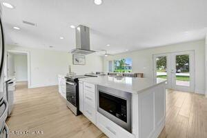 57 Riverview Ln, Cocoa Beach, FL 32931 - kitchen featuring stainless steel appliances, wall chimney exhaust hood, light wood-style floors, light countertops, and french doors