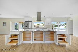 57 Riverview Ln, Cocoa Beach, FL 32931 - kitchen with wall chimney exhaust hood, freestanding refrigerator, white cabinets, light wood-type flooring, and light countertops