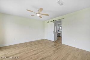 57 Riverview Ln, Cocoa Beach, FL 32931 - unfurnished room featuring wood finished floors, a barn door, and ceiling fan