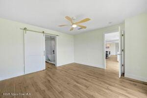 57 Riverview Ln, Cocoa Beach, FL 32931 - unfurnished bedroom featuring a barn door, wood finished floors, and a ceiling fan