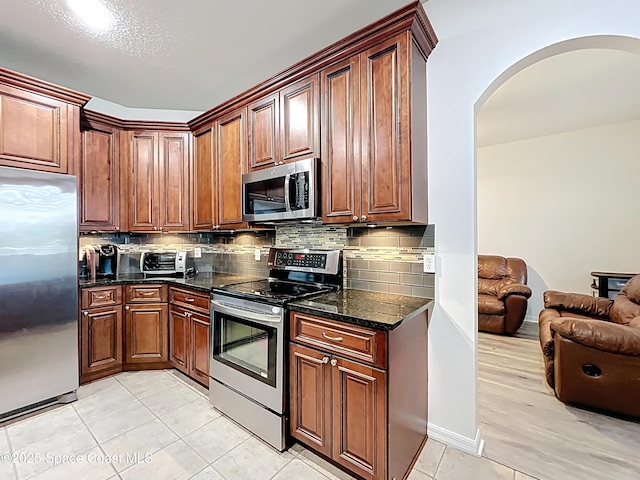 9525 Southern Garden Cir, Altamonte Springs, FL 32714 - kitchen with stainless steel appliances, arched walkways, light tile patterned floors, dark stone counters, and backsplash