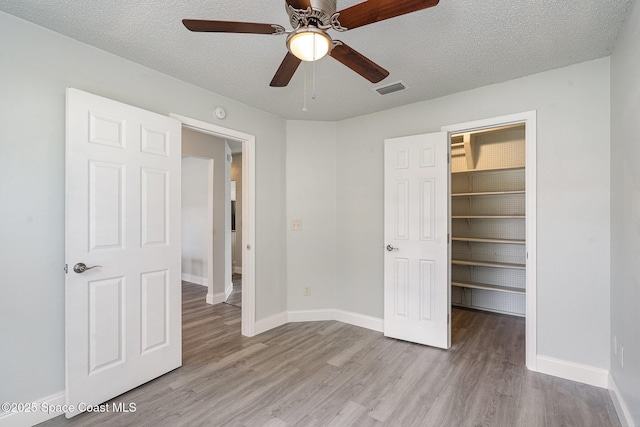 542 White Plains Ave SW, Palm Bay, FL 32908 - unfurnished bedroom featuring a walk in closet, wood finished floors, baseboards, a closet, and a textured ceiling