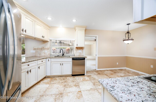 630 Seville Ct, Satellite Beach, FL 32937 - kitchen with appliances with stainless steel finishes, light stone countertops, wainscoting, hanging light fixtures, and decorative backsplash