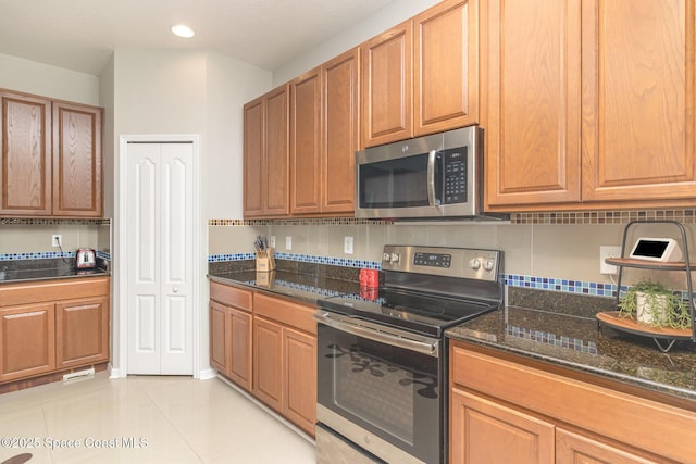 2039 Snapdragon Dr NW, Palm Bay, FL 32907 - kitchen featuring appliances with stainless steel finishes, dark stone countertops, light tile patterned floors, tasteful backsplash, and brown cabinetry