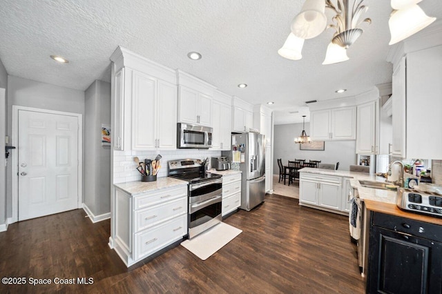 1236 Foxridge Pl, Melbourne, FL 32940 - kitchen with stainless steel appliances, a chandelier, white cabinets, dark wood-style floors, and recessed lighting