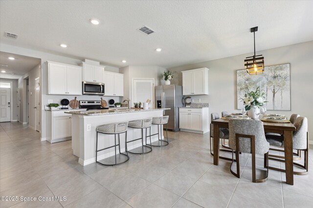 1103 Dunes Ave, Melbourne, FL 32904 - kitchen featuring stainless steel appliances, a kitchen island with sink, a breakfast bar, white cabinetry, and recessed lighting
