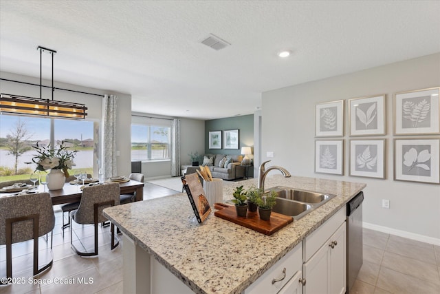 1103 Dunes Ave, Melbourne, FL 32904 - kitchen with stainless steel dishwasher, open floor plan, a center island with sink, white cabinetry, and light stone countertops