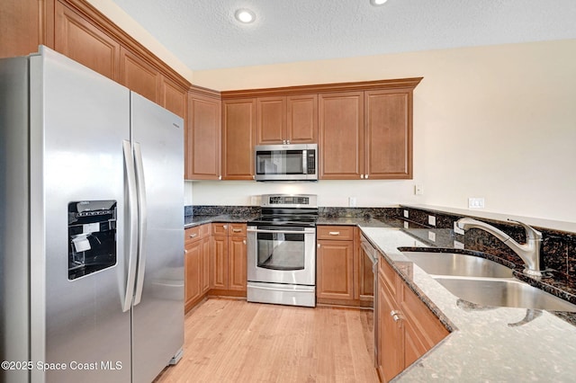 2178 Tanager Ct, Melbourne, FL 32903 - kitchen featuring stainless steel appliances, a sink, light wood-style flooring, dark stone counters, and a textured ceiling