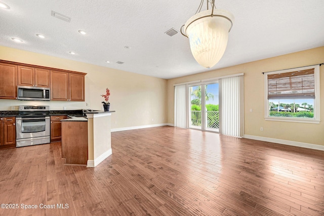 2178 Tanager Ct, Melbourne, FL 32903 - kitchen with stainless steel appliances, dark countertops, brown cabinets, open floor plan, and wood finished floors