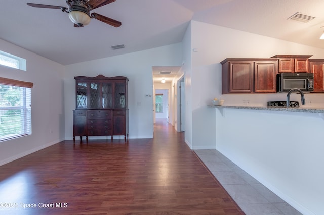 4180 Seville Ave, Cocoa, FL 32926 - kitchen featuring black microwave, wood finished floors, ceiling fan, light stone counters, and high vaulted ceiling