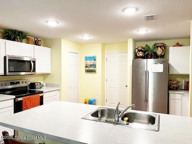 1119 Blossom Dr, Sebastian, FL 32958 - kitchen featuring appliances with stainless steel finishes, a textured ceiling, a sink, white cabinets, and light countertops