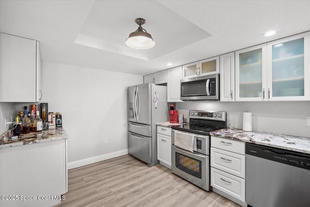 530 S Brevard Ave Unit 315, Cocoa Beach, FL 32931 - kitchen featuring stainless steel appliances, a raised ceiling, white cabinets, light wood-style flooring, and light stone counters