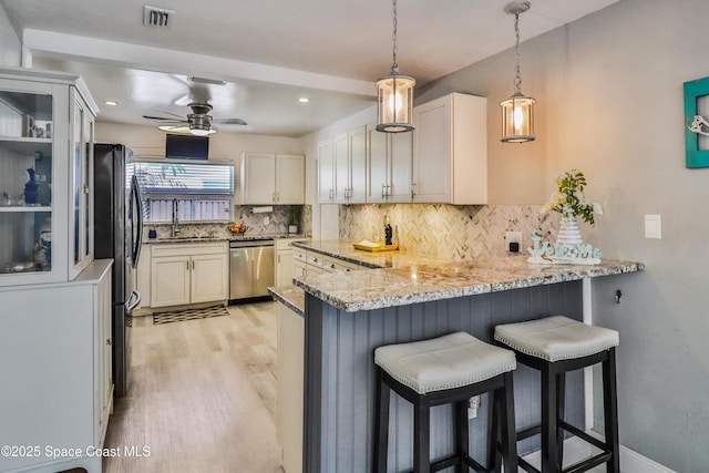 348 Berkeley St, Satellite Beach, FL 32937 - kitchen with appliances with stainless steel finishes, a peninsula, light wood-style flooring, decorative backsplash, and light stone countertops
