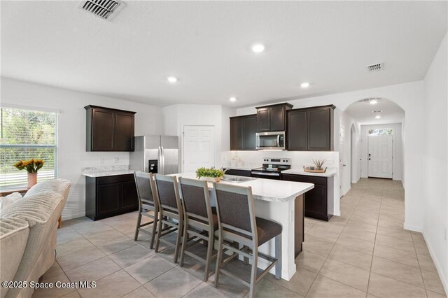1093 Wabash Rd SE, Palm Bay, FL 32909 - kitchen featuring appliances with stainless steel finishes, light countertops, arched walkways, light tile patterned flooring, and dark brown cabinets