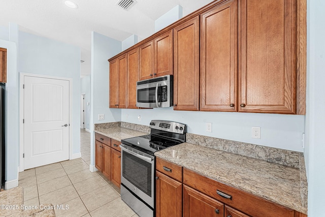 1121 S Orlando Ave, Cocoa Beach, FL 32931 - kitchen featuring stainless steel appliances, brown cabinets, light tile patterned flooring, and light stone countertops