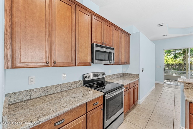 1121 S Orlando Ave, Cocoa Beach, FL 32931 - kitchen featuring appliances with stainless steel finishes, brown cabinetry, light tile patterned floors, and light stone counters