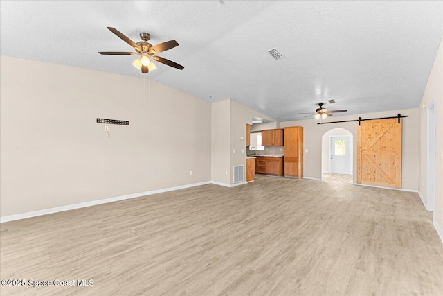 5510 Holden Rd, Cocoa, FL 32927 - unfurnished living room with a ceiling fan, light wood-style flooring, a textured ceiling, a barn door, and vaulted ceiling