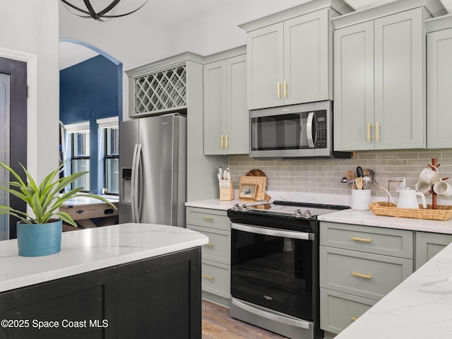 3662 Brantley Cir, Rockledge, FL 32955 - kitchen featuring appliances with stainless steel finishes, tasteful backsplash, light stone counters, wood finished floors, and arched walkways