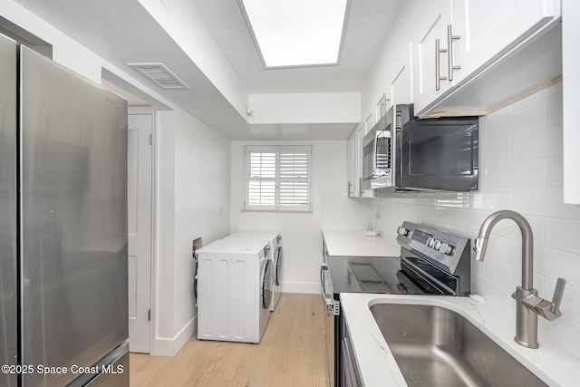 170 Paradise Blvd # 17, Indialantic, FL 32903 - kitchen featuring appliances with stainless steel finishes, washer and dryer, light wood-style floors, white cabinets, and backsplash