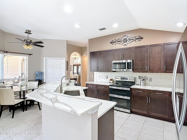 603 Cross Creek Dr, Sebastian, FL 32958 - kitchen featuring stainless steel appliances, light tile patterned floors, vaulted ceiling, a kitchen island with sink, and decorative backsplash