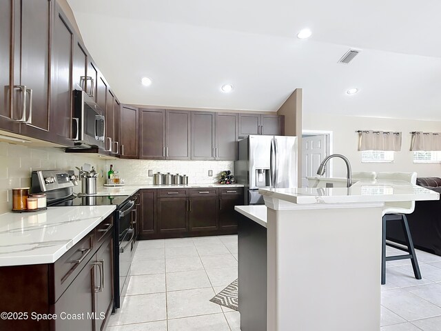 603 Cross Creek Dr, Sebastian, FL 32958 - kitchen with appliances with stainless steel finishes, light tile patterned flooring, a kitchen breakfast bar, dark brown cabinets, and decorative backsplash