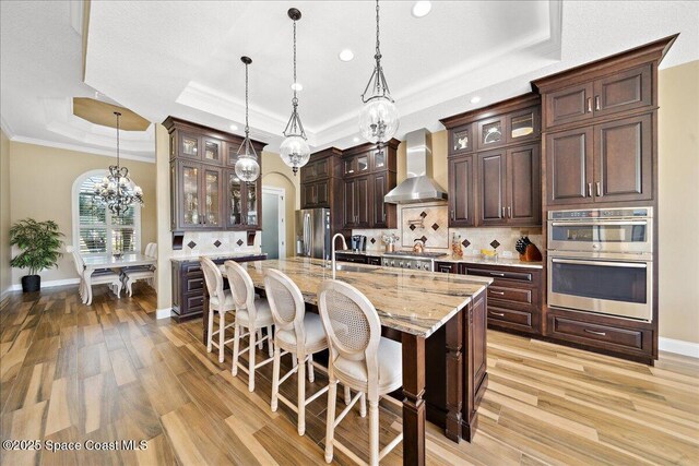 4464 Preservation Cir, Melbourne, FL 32934 - kitchen with wall chimney exhaust hood, a raised ceiling, appliances with stainless steel finishes, a chandelier, and dark brown cabinetry