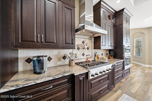 4464 Preservation Cir, Melbourne, FL 32934 - kitchen with wall chimney range hood, stainless steel appliances, dark brown cabinets, light stone countertops, and backsplash