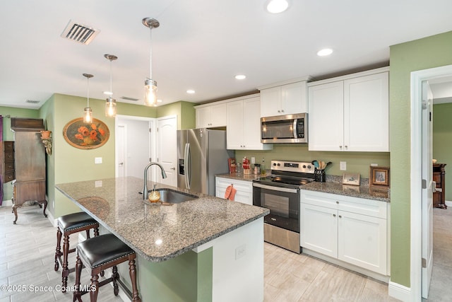 950 Douglas St SE, Palm Bay, FL 32909 - kitchen featuring stainless steel appliances, white cabinets, a kitchen island with sink, a kitchen breakfast bar, and dark stone countertops