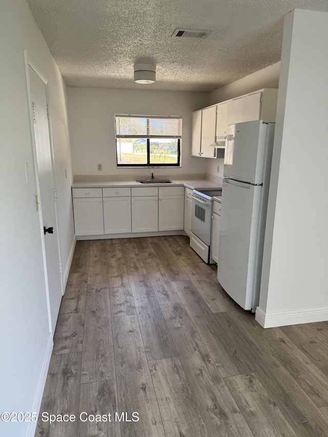 1112 Wabash Rd SE, Palm Bay, FL 32909 - kitchen featuring white appliances, white cabinets, wood finished floors, a textured ceiling, and light countertops