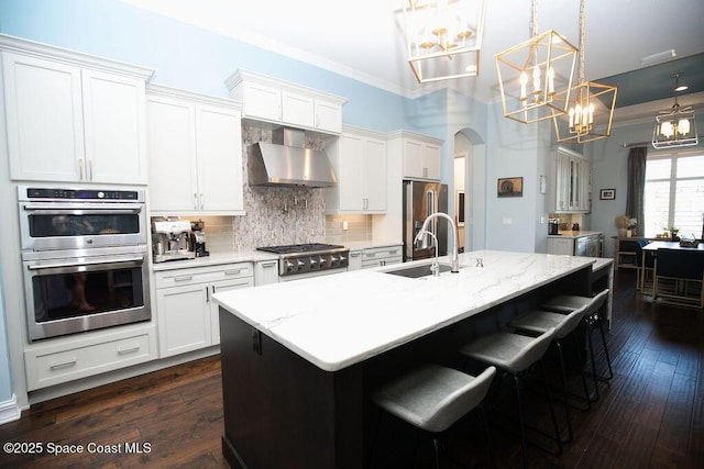 7354 Lucaya Ct, Melbourne, FL 32940 - kitchen with wall chimney range hood, appliances with stainless steel finishes, a chandelier, arched walkways, and tasteful backsplash