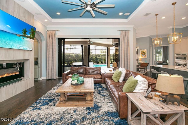 7354 Lucaya Ct, Melbourne, FL 32940 - living area with dark wood-style floors, a ceiling fan, ornamental molding, a tray ceiling, and a glass covered fireplace
