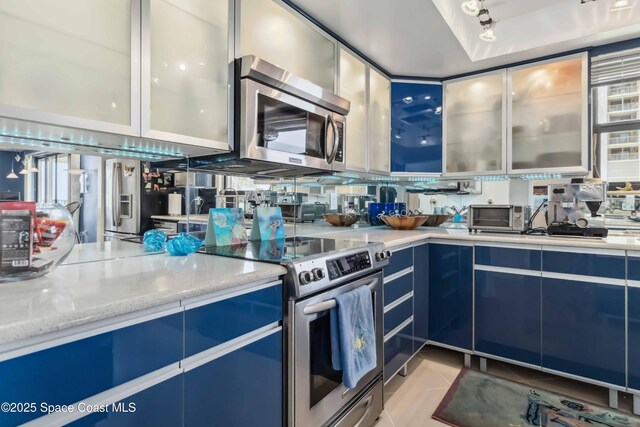 750 N Atlantic Ave Unit 203, Cocoa Beach, FL 32931 - kitchen with appliances with stainless steel finishes, blue cabinets, glass insert cabinets, and light stone countertops