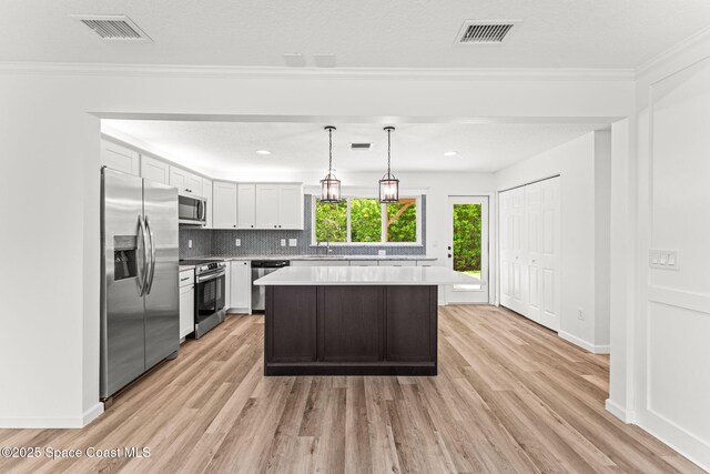 332 Nikomas Way, Melbourne Beach, FL 32951 - kitchen with appliances with stainless steel finishes, light countertops, light wood-type flooring, a center island, and crown molding