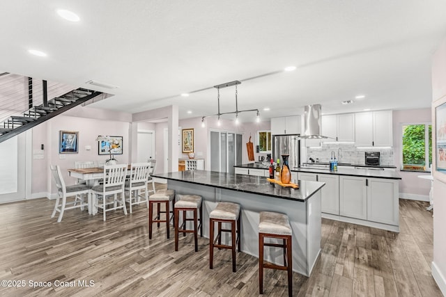 1379 Rose Ct, Melbourne, FL 32935 - kitchen with a center island, wall chimney exhaust hood, dark countertops, wood finished floors, and freestanding refrigerator
