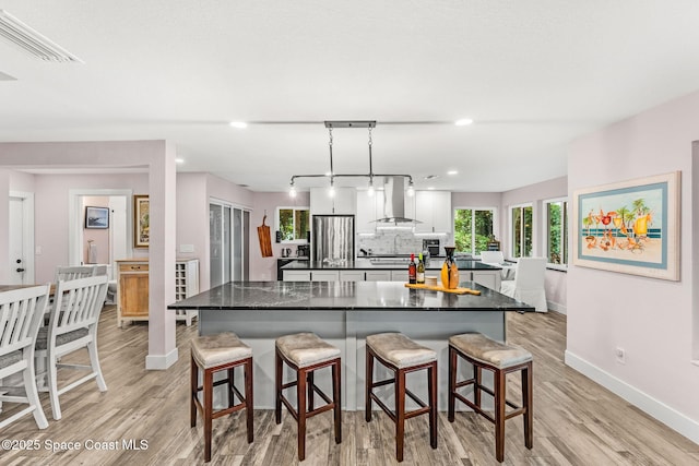 1379 Rose Ct, Melbourne, FL 32935 - kitchen featuring wall chimney range hood, freestanding refrigerator, a large island, dark countertops, and light wood-type flooring