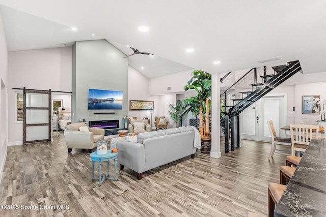 1379 Rose Ct, Melbourne, FL 32935 - living area with stairs, high vaulted ceiling, light wood-style floors, a barn door, and a glass covered fireplace