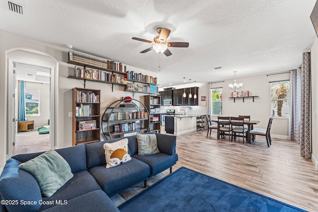 2920 Casterton Dr, Melbourne, FL 32940 - living room with a textured ceiling, light wood-style floors, a ceiling fan, arched walkways, and a chandelier