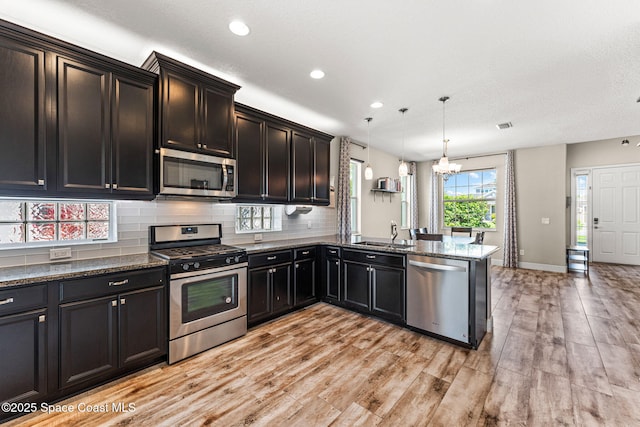 2920 Casterton Dr, Melbourne, FL 32940 - kitchen featuring stainless steel appliances, a chandelier, a peninsula, dark stone countertops, and light wood-type flooring