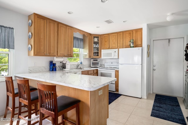 61 Woodland Dr Unit 201, Vero Beach, FL 32962 - kitchen featuring white appliances, a peninsula, light countertops, brown cabinetry, and glass insert cabinets
