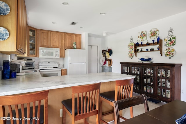 61 Woodland Dr Unit 201, Vero Beach, FL 32962 - kitchen with white appliances, a peninsula, brown cabinets, glass insert cabinets, and a kitchen bar