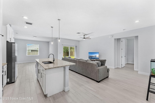 443 Archer Rd SE, Palm Bay, FL 32909 - kitchen with stainless steel fridge, light wood finished floors, a ceiling fan, white cabinetry, and a kitchen island with sink